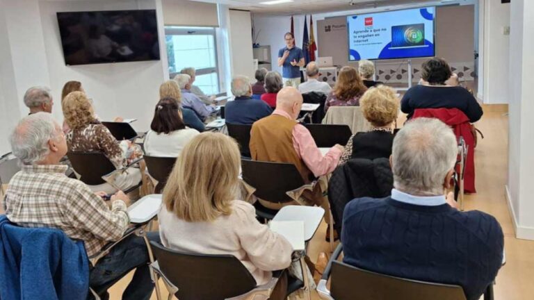 Personas asistiendo a un curso de competencias digitales en un aula, con un formador explicando cómo navegar en internet de forma segura.